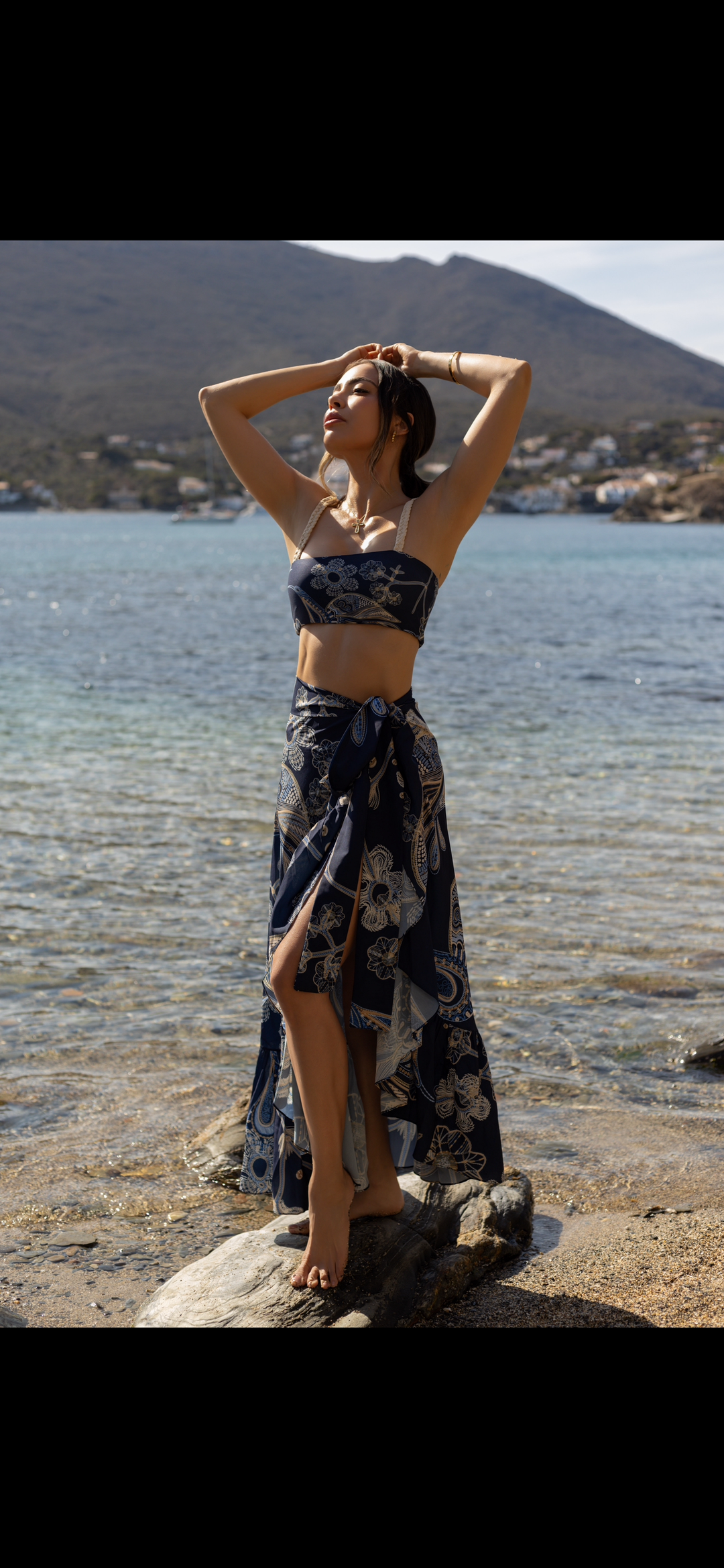 Montecarlo Two-Piece Swimsuit in navy and gold print, featuring a bandeau top and high-waisted bottom, modeled by the ocean.