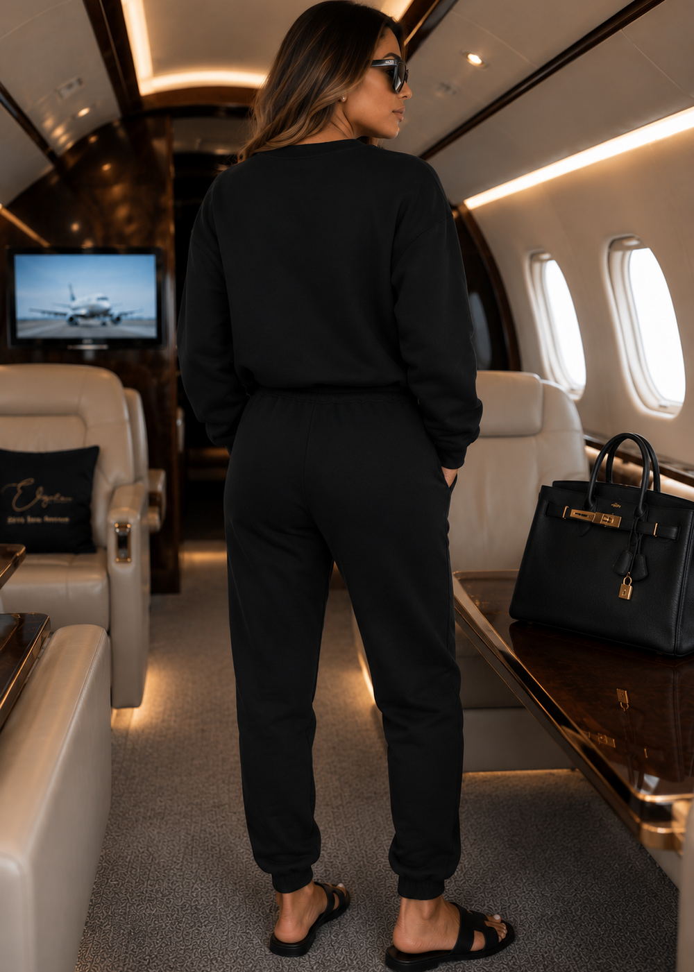 Back view of the black three-piece luxury jogger set with a clean, logo-free back design, photographed inside a private jet to showcase premium travel style and effortless comfort.