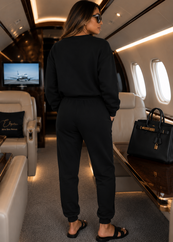 Back view of the black three-piece luxury jogger set with a clean, logo-free back design, photographed inside a private jet to showcase premium travel style and effortless comfort.