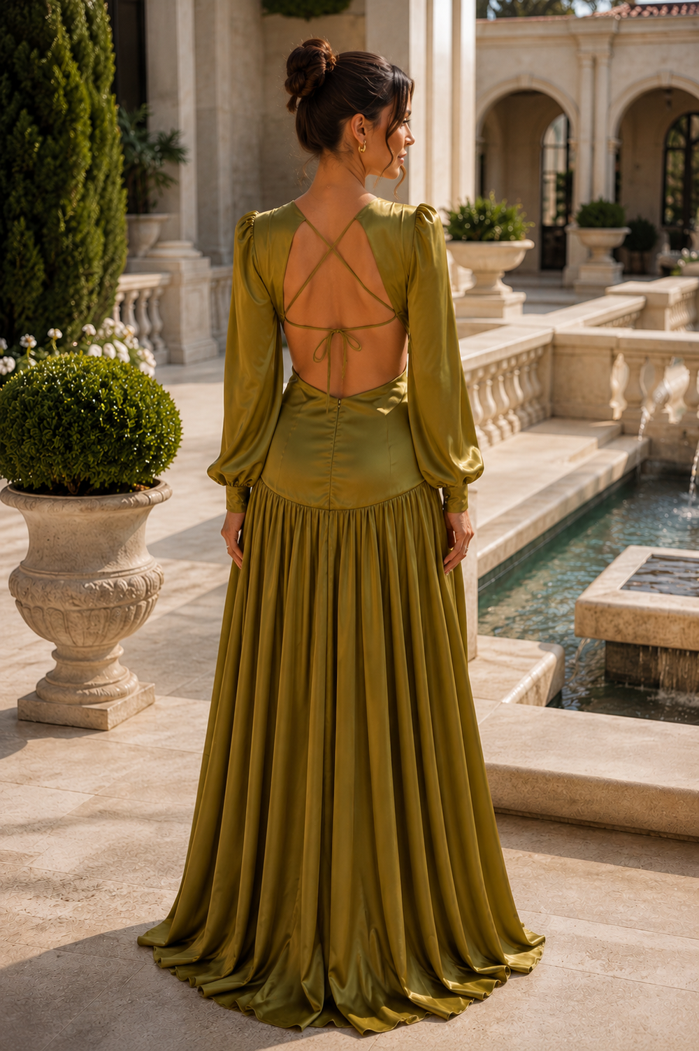 Back view of the Mykonos Olive Green Cutout Long Sleeve Satin Maxi Dress showcasing the open-back design with delicate tie details, flowing satin skirt, and elegant silhouette in a luxury Mediterranean outdoor setting.
