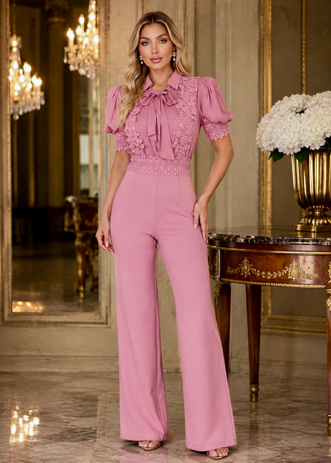 Luxury blonde model wearing the Norma Pink Organza Jumpsuit with sheer ruffle blouse, high waist and wide-leg pants in an elegant palace-inspired interior.