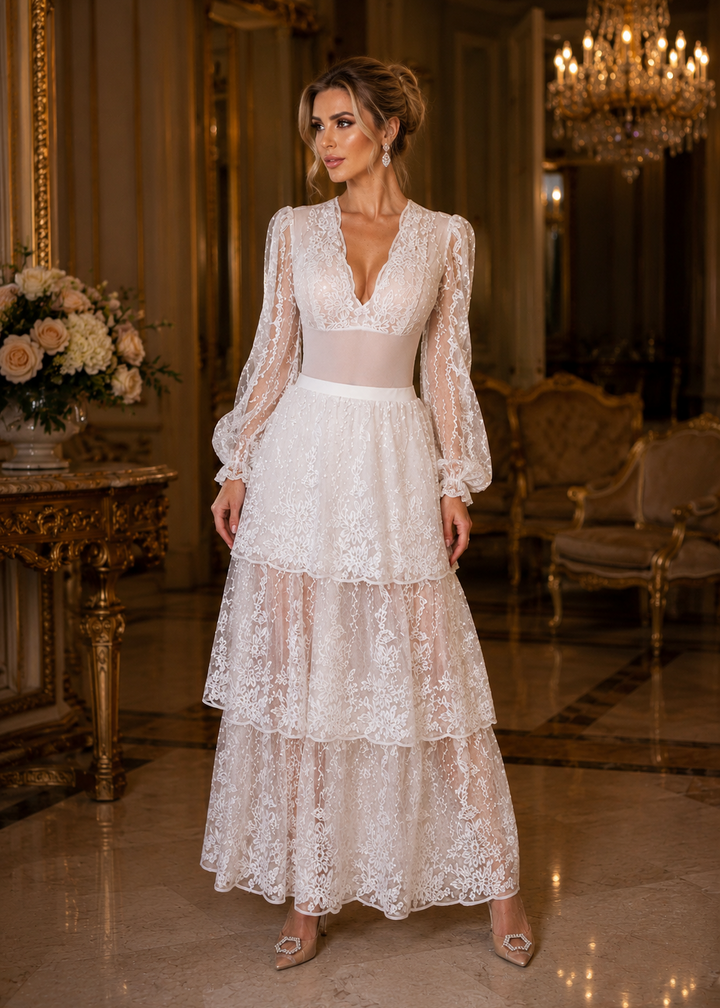 Woman wearing the ODETTE White 2-Piece Lace Body Suit &amp; Skirt featuring embroidered lace, sheer long sleeves, a tiered skirt, and elegant crystal details in a luxurious ballroom.