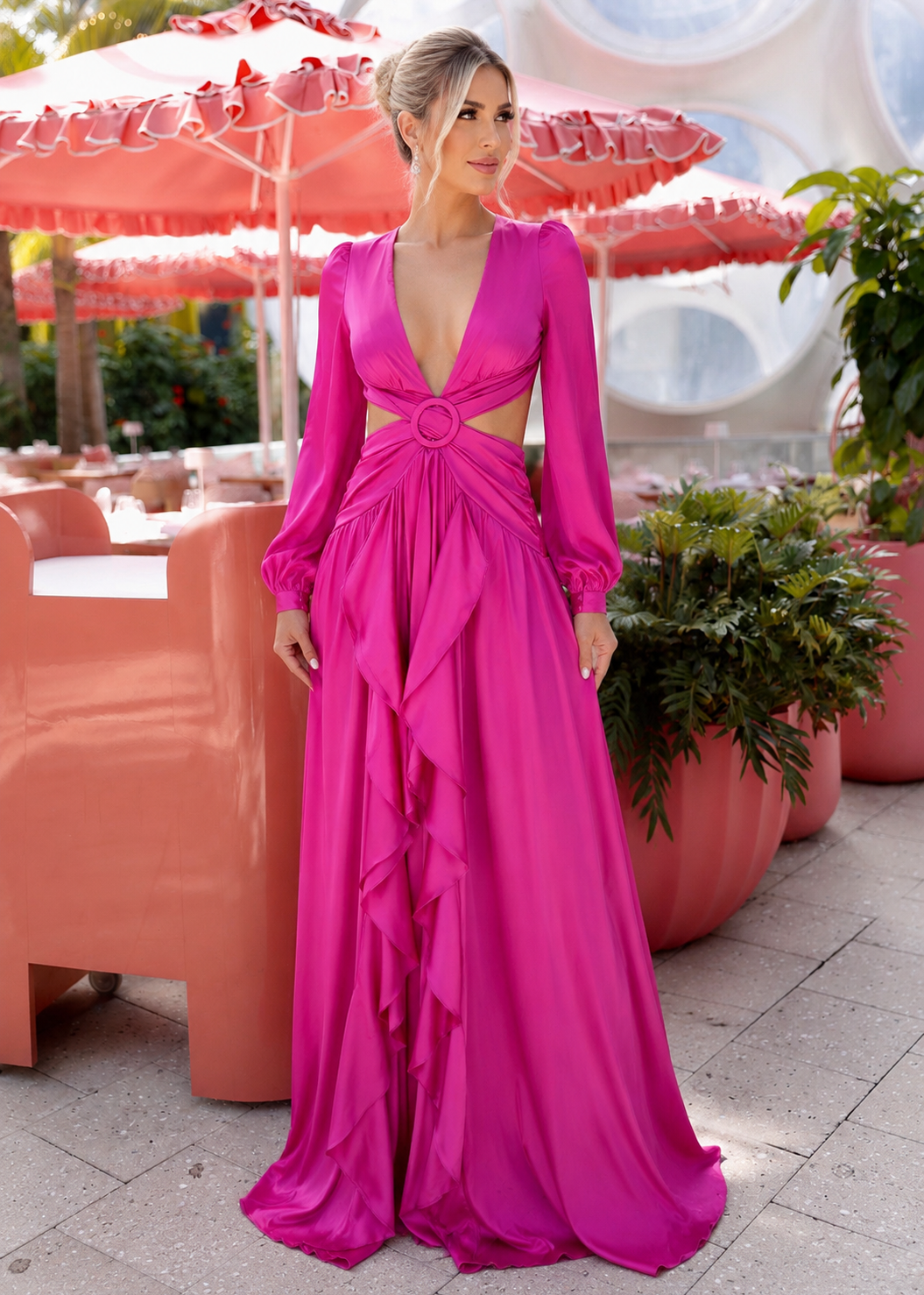 Woman wearing the Mykonos Fuchsia Cutout Long Sleeve Satin Maxi Dress in a luxury outdoor resort setting with elegant satin fabric and flowing silhouette.